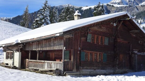 A rustic wooden cabin with a snow-covered roof, set against a backdrop of snow-covered mountains and evergreen trees. - Hami Appartement/Fewo, Dusche, WC, 3 Schlafräume Bauernhaus by Interhome (Adelboden)