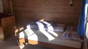 A wooden cabin bedroom with a bed, a dresser, and a window with curtains. - Hami Appartement/Fewo, Dusche, WC, 3 Schlafräume Bauernhaus by Interhome (Adelboden)