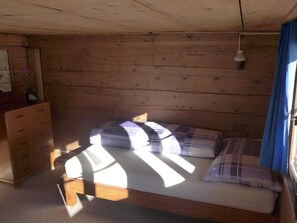 Ein Schlafzimmer einer Holzhütte mit einem Bett, einem Schminktisch und einem Fenster mit Vorhängen.