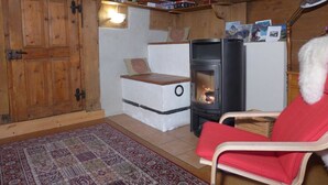 A cozy room with a wood-burning stove, a red chair, and a patterned rug. - Hami Appartement/Fewo, Dusche, WC, 3 Schlafräume Bauernhaus by Interhome (Adelboden)