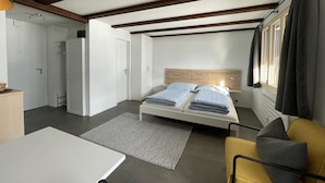 Una habitación compacta con cama, una mesita, un sofá y una ventana con cortinas.