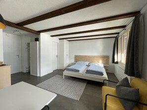 Een knus slaapkamer met een bed, een klein tafeltje, een bank en een raam met gordijnen.