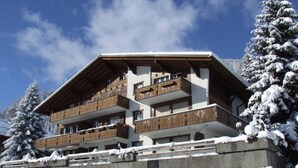 Un edificio de varios pisos con balcones, rodeado de árboles cubiertos de nieve, bajo un cielo despejado.