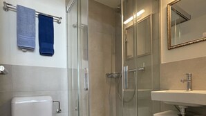 Un baño moderno con ducha envuelta en vidrio, inodoro, lavamanos y espejo.
