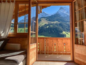 A wooden cabin with a large window offering a mountain view.
