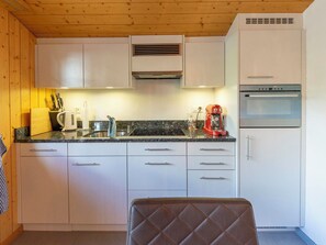 A compact kitchen with white cabinets, a granite countertop, a coffee maker, and a built-in oven.