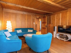 A room with wooden walls and ceiling, a blue sofa set, a flat-screen TV on a white stand, and a small table. - Im Zentrum Appartement/Fewo, Dusche und Bad, WC, 2 Schlafräume 3-Zimmerwohnung by Interhome (Adelboden)