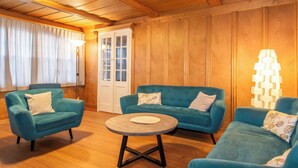 Ein gemütliches Zimmer mit Holzwänden und -decke, ausgestattet mit zwei blauen Sofas, einem runden Couchtisch und einer Tür mit Glasverkleidung.