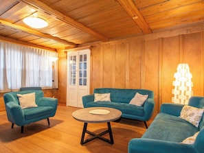 Ein gemütliches Zimmer mit Holzwänden und -decke, ausgestattet mit zwei blauen Sofas, einem runden Couchtisch und einer Tür mit Glasverkleidung.