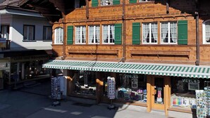 Ein traditionelles Holzgebäude mit grüner Markise, einem sichtbaren Schaufenster und einem Berg im Hintergrund.