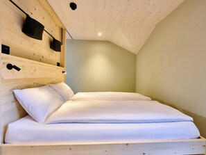 Quarto com cabeceira de madeira, cama com roupa de cama branca e parede em tom claro.