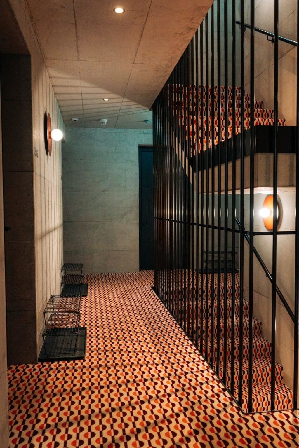 Un passadís amb paviment decoratiu, una escala amb graons motius i una barana metàl·lica.