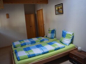 Ein Zimmer mit einem Einzelbett, einem Holzkopfstück, einer grün-blauen Karomatik und einem Nachttisch mit einer Lampe.