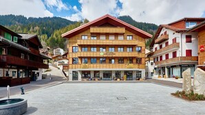 Un hotel a più piani con facciata in legno, un cortile centrale e le montagne sullo sfondo.