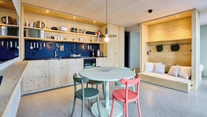 Una cucina moderna con mobili in legno, un tavolo da pranzo con sedie e un'area salotto integrata con cuscini.