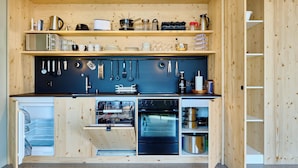 Una cucina compatta con mobili in legno, forno integrato e diversi utensili ed elettrodomestici.