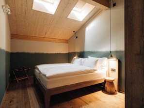 Un dormitorio con techo inclinado, tragaluces, una cama, mesita de noche y lámpara colgante.