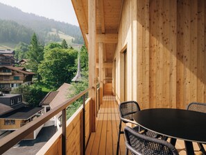 Ein Holzbalkon mit Tisch und Stühlen, mit Blick auf ein Dorf und bewaldete Hügel.