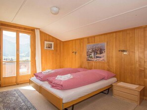 Une chambre à coucher avec un lit en bois, une petite table de chevet, une fenêtre donnant sur un beau paysage et un tableau accroché au mur.