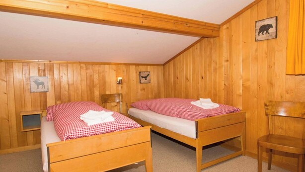 Ein Zimmer mit zwei hölzernen Betten, einem Sessel und einem kleinen Tisch.