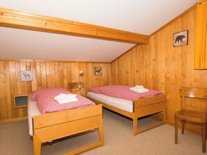 Ein Zimmer mit zwei hölzernen Betten, einem Sessel und einem kleinen Tisch.