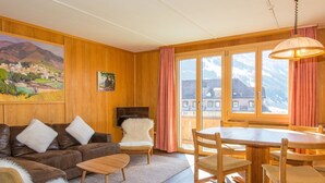 Ein gemütliches Wohnzimmer mit einer braunen Ledersofa, einem weißen, flauschigen Sessel, einem Holztisch und einem Essbereich mit Esstisch und Stühlen.