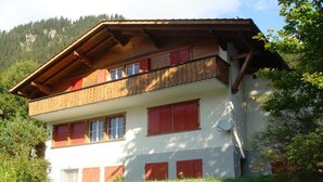 Ein zweistöckiges Gebäude mit einem hölzernen Balkon, roten Fensterläden und einer weißen Fassade.