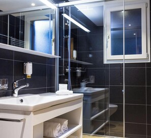 Een moderne badkamer met een douchecabine van glas, een witte wastafel en een spiegel.