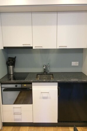Cocina compacta con armarios blancos, lavavajillas de acero inoxidable, horno integrado y encimera de granito.