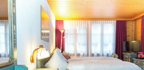Een hotelkamer met een bed, een nachtkastje met een lamp, een spiegel en een raam met gordijnen.