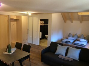 A modern living room with a sofa, a dining table, and a kitchen area visible in the background. - Hotel Bären Appartement/Fewo, Dusche, WC, 1 Schlafraum Studio - Nebenhaus by Interhome (Adelboden)