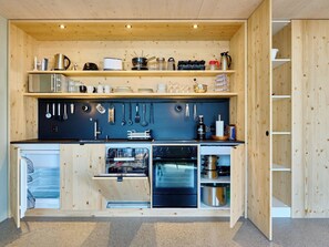 Eine kleine Küche mit Holzschränken, einem eingebauten Ofen sowie verschiedenen Kochutensilien und Geräten.