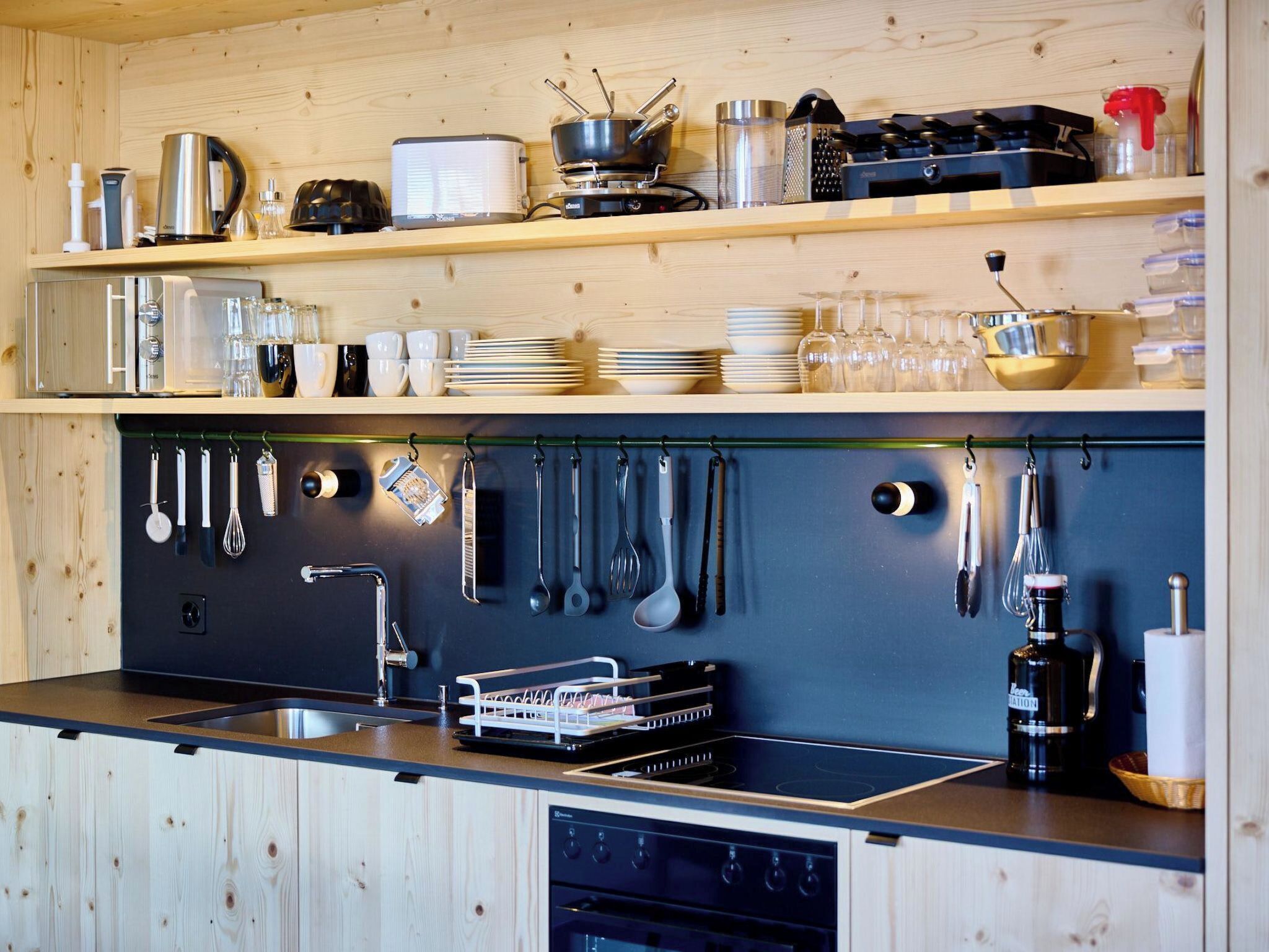 Een keuken met houten kastjes, een roestvrijstalen spoelbak en diverse keukengerei aan de wand.