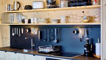 Een keuken met houten kastjes, een roestvrijstalen spoelbak en diverse keukengerei aan de wand.