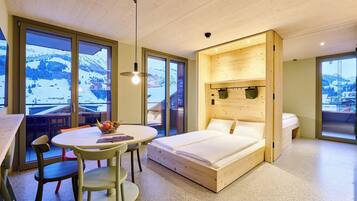 Een moderne kamer met een bed, een tafel en stoelen, grote ramen met uitzicht op een besneeuwde berg, en houten wanden.