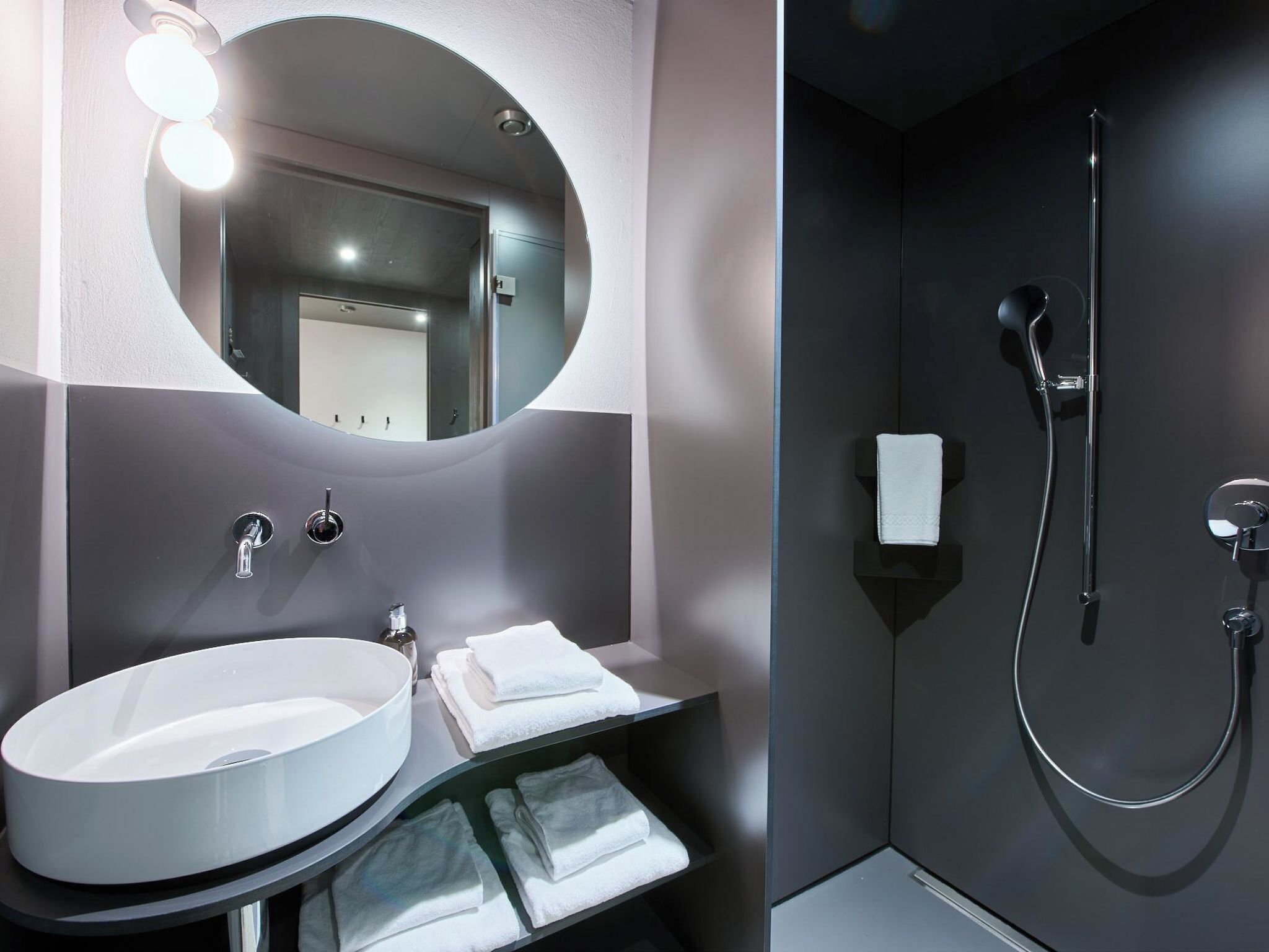 A modern bathroom with a round mirror, a sink, and a shower.