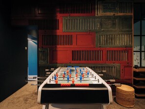 A foosball table in a room with a red and green wall paneling, a blue door, and a woven basket. - KURVE Apartments & Lounge Appartement/Fewo, Bad, WC, 2 Schlafräume by Interhome (Adelboden)