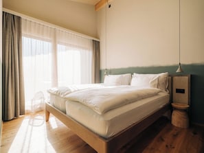 A bedroom with a wooden bed, a nightstand, a lamp, and a window with curtains. - KURVE Apartments & Lounge Appartement/Fewo, Bad, WC, 2 Schlafräume by Interhome (Adelboden)