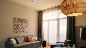 A modern living room with a grey sofa, a round wooden table with bottles, a woven light fixture, and a large window with curtains. - KURVE Apartments & Lounge Appartement/Fewo, Bad, WC, 2 Schlafräume by Interhome (Adelboden)