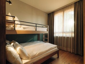 Ein Schlafraum mit Etagenbetten, einem Schreibtisch und einem Fenster mit Vorhängen.