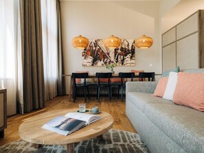 A modern living room with a round wooden coffee table, a grey sofa with pink cushions, and a dining area with chairs and a table. - KURVE Apartments & Lounge Appartement/Fewo, Bad, WC, 3 Schlafräume by Interhome (Adelboden)