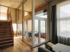 Ein modernes Interieur mit einer Holztreppe, großen Glasüren, die zu einem Außenbereich führen, und Blick ins Freie.