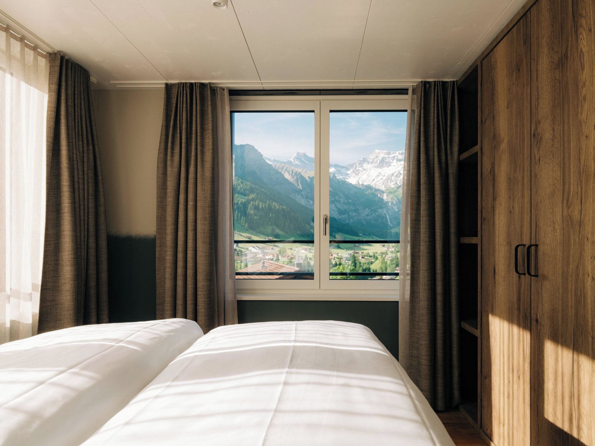 Habitación de hotel con cama, ventana y vistas a la montaña, además de un armario de madera.