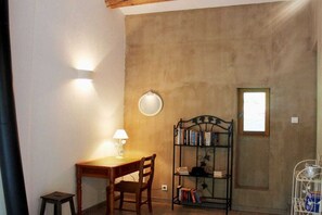 Ein Zimmer mit einem Holztisch und Stuhl, einem Bücherregal, einem runden Wandspiegel und einem Fenster.
