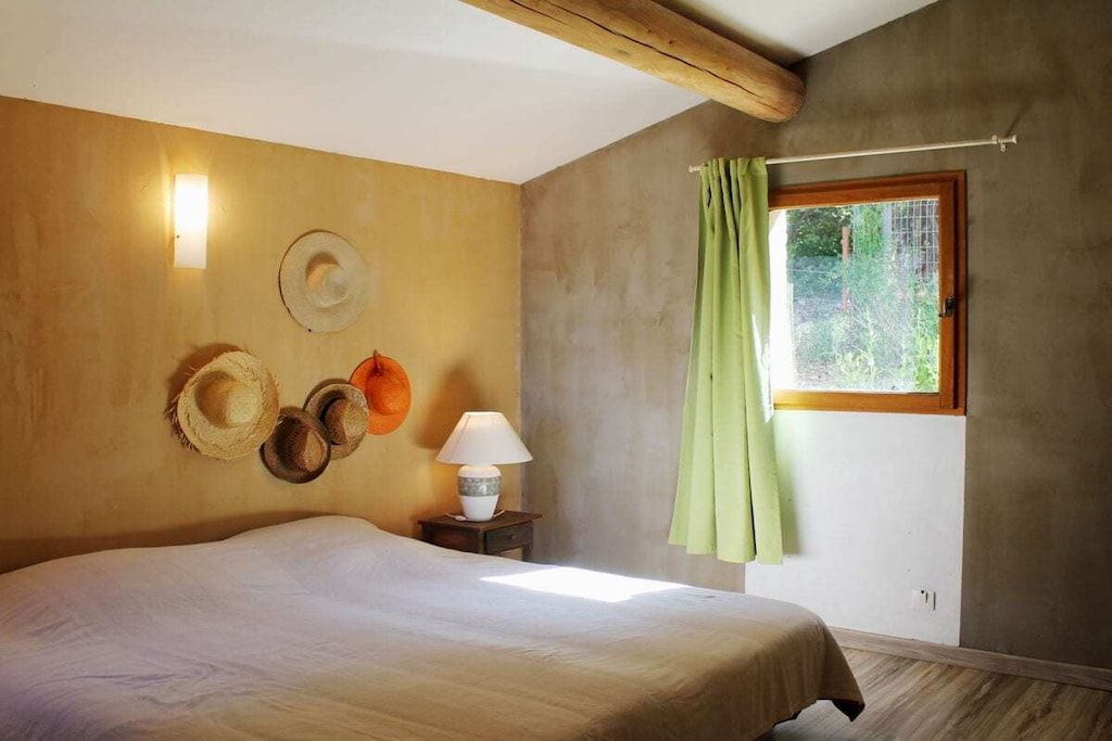 Un dormitorio con cama, mesita de noche, lámpara y ventana con cortinas.