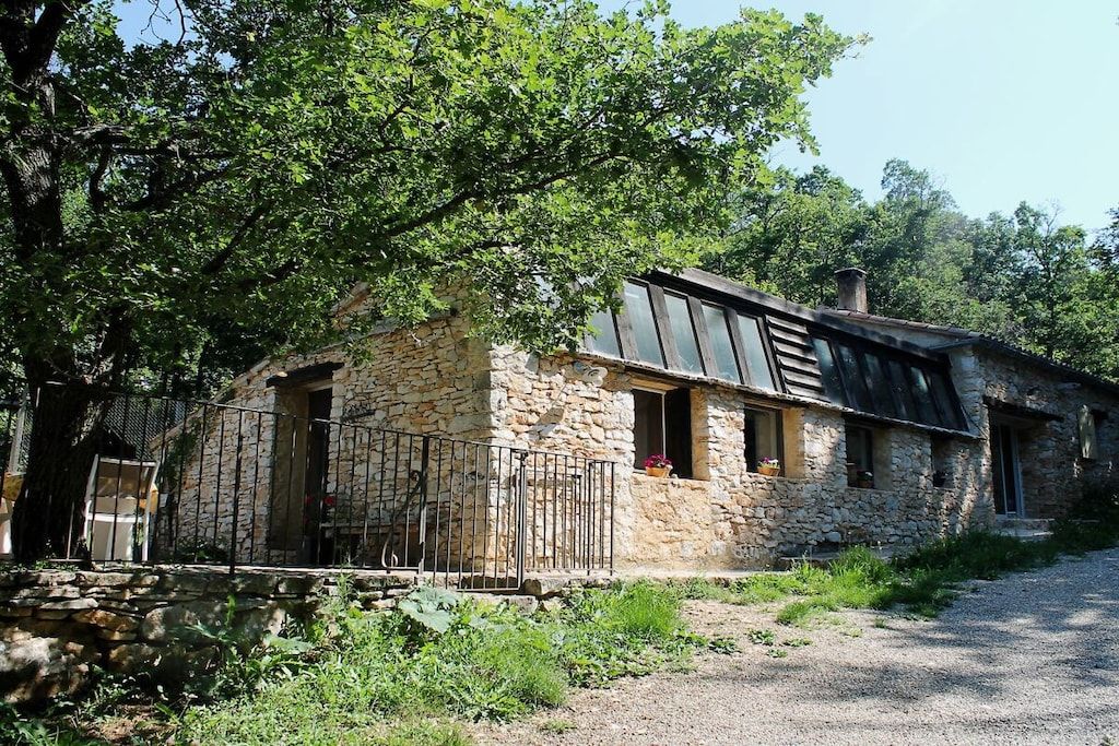 A stone building with a metal roof, a gravel driveway, and a metal fence.