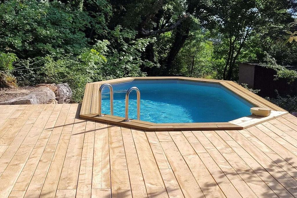 A wooden deck with a rectangular swimming pool, surrounded by trees.