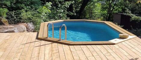 A wooden deck with a rectangular swimming pool, surrounded by trees.