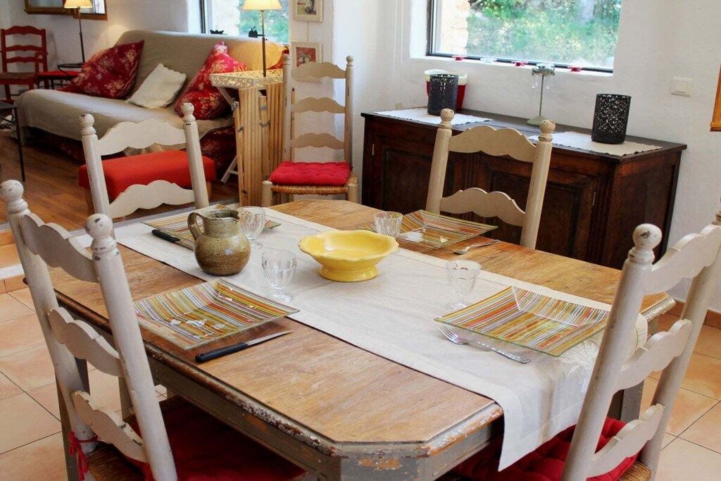 Une table à manger dressée avec des assiettes, des verres et un pichet, entourée de chaises à la finition blanche.
