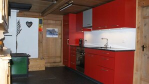 A kitchen with red cabinets, a black countertop, and a stove. - Heuzündli Ferienhaus, Dusche, WC, 3 Schlafräume 4-Zimmer-Ferienhaus by Interhome (Adelboden)